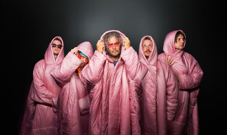 Promotional portrait of American rock band The Flaming Lips wearing matching hooded pink oversized coats.